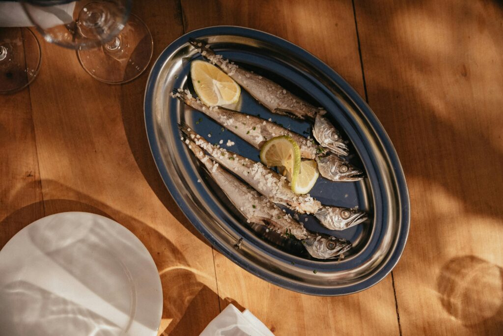 Freshly grilled fish garnished with lemon slices and coarse salt served on a wooden table.