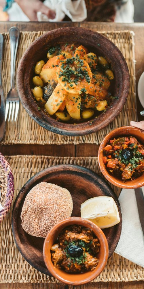 Delicious Moroccan dishes served with fresh vegetables and traditional bread on a woven mat.